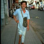 Young man with a withered leg due to polio outside on a sidewalk, using a cane.