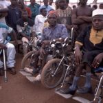 Two men in wheelchairs, with a crowd of other polio patients.